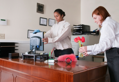 Two cleaning staff members cleaning an office. One is in training